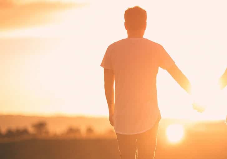 man holding hands with someone and staring at the sunrise