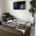 comfortable living area for patients at the Denver Detox Center with leather couches and chairs, a television is hung on the wall and a large potted plant is in the corner