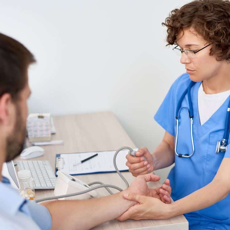 Portrait of young woman measuring patients blood pressure at desk in doctors office